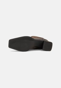 Brown leather shoe with a textured black rubber sole and a block heel. The sole features horizontal grooves for traction.