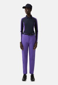 Tmavě modré polo tričko s dlouhým rukávem s fialovými akcenty, doplněné fialovými kalhotami a černými botami. Outfit je doplněn tmavě modrou čepicí.