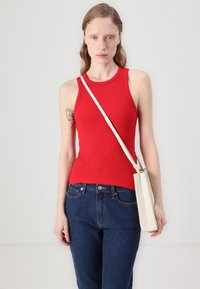 Rød ribbestrikket tanktop med en tettsittende silhuett, kombinert med mørk denimjeans. En hvit crossover-veske bæres på den ene skulderen.