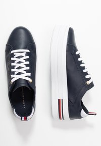 Baskets en cuir bleu marine avec lacets blancs, œillets dorés, semelles blanches épaisses et accents rayés rouges et blancs sur le talon.