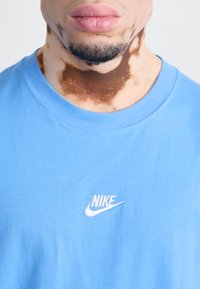 Gaiši zils kokvilnas T-krekls ar baltu izšūtu Nike logo kreisajā krūšu daļā. Klasiska apaļā kakla dizaina ar gludu tekstūru.
