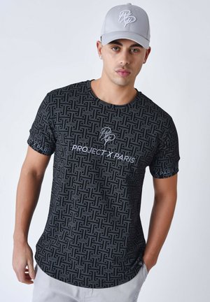 Camiseta negra de manga corta con un patrón geométrico, que presenta el texto blanco "PROJECT X PARIS" en la parte delantera y en las mangas. Gorra gris.