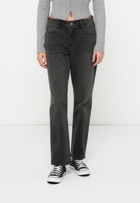 Črne denim hlače s ravnim krojem, ki imajo pet žepov, kontrastno šivanje in zadrgo; obute s črnimi supergami.