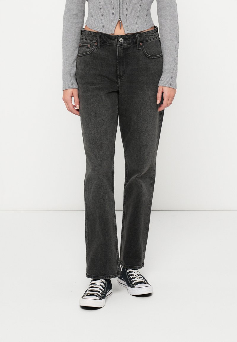 Črne denim hlače s ravnim krojem, ki imajo pet žepov, kontrastno šivanje in zadrgo; obute s črnimi supergami.