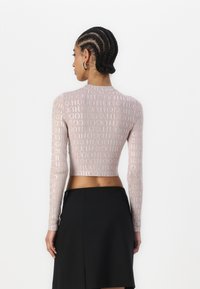 Lys rosa langermet topp med cropped snitt, med et gjentatt logo-mønster og rund hals, paret med et svart skjørt.