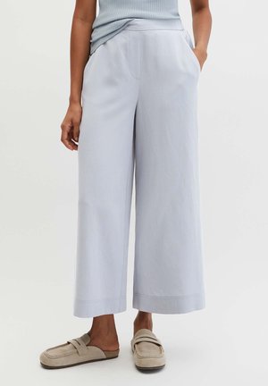 Donna che indossa pantaloni corti a zampa d'elefante color azzurro chiaro con tasche, abbinati a mocassini beige senza lacci.