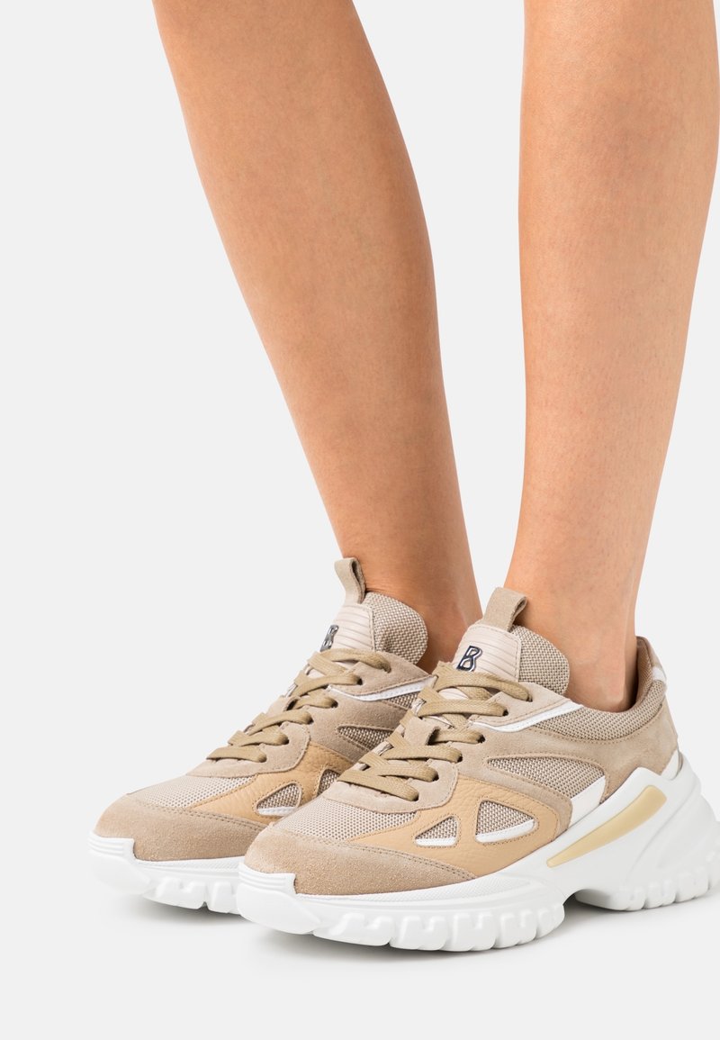 Sneakers beige con un mix di materiali in suede e mesh. Suola bianca chunky, colletto imbottito e sistema di allacciatura prominente. Design a ritaglio notevole.