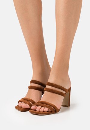 Sandales à talons en suède marron avec trois larges bandes à l'avant des orteils et un talon épais. La semelle est plate et le design est ouvert à l'arrière.