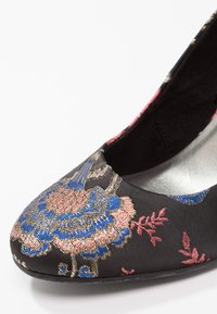 Chaussure en tissu noir avec broderie florale en rose, bleu et or. Caractérisée par un bout arrondi et un design latéral ouvert. Doublure intérieure lisse.