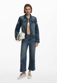 Jeansjacka och cropade jeans med blommönster, i mörkblått. Vita sneakers, håller en liten vit handväska. Avslappnad outfit.