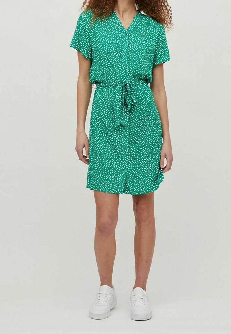 Grön kortärmad klänning med V-ringning och vita prickar, med en upptagen midja och knappar fram, tillsammans med vita sneakers.