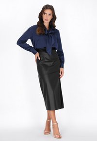 Mørkeblå satinbluse med buebind, parret med en sort faux læder midi-nederdel med en sideslids og strappy klare hæle.