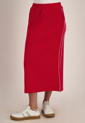Rode midi-rok met zijzakken en witte strepen, gedragen met witte sneakers op een neutrale achtergrond.