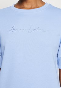 Ljusblå sweatshirt med ribbat krage och korta ärmar, med "Armani Exchange" broderat i kursiv över bröstet.