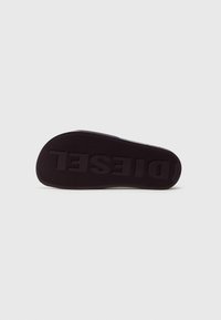 Black rubber shoe sole with textured grip, featuring a branded logo and a rounded shape. Clean lines with a minimalist design.
