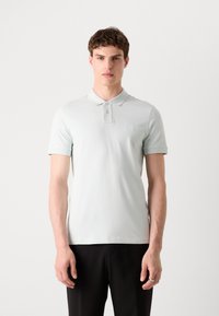 Svetle modrá polo košile vyrobená z bavlny, s klasickým límečkem, tři knoflíky a malou nášivkou s logem na prsou.