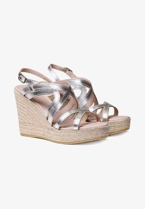 Sandales compensées argentées à brides avec boucles à la cheville et talons compensés en corde tressée, présentées côte à côte sur un fond blanc.
