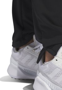 Vitaidrottsskor i vitt med meshmaterial, som har tre sidostråk, en vadderad krage och gummisålar. Svarta byxor med en tajt mudd.