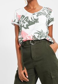 Lyhythihainen, V-pääntievalkoinen paita, jossa on vihreitä ja vaaleanpunaisia trooppisia lehtikuvioita. Sisältää pienen valkoisen rintataskun. Yhdistetty oliivinvihreisiin cargo-housuihin.