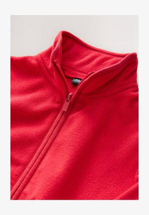 Piros polárdzseki magas gallérral és cipzárral. Simább tapintású anyag, varrással díszítve, a gallér belsejében látható címkével.