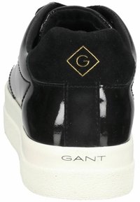 Zapatilla negra con una combinación de charol y ante. Suela texturizada blanca y acento dorado del logo en el talón. Diseño simple y moderno.