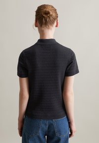 Zwarte gestructureerde polo met korte mouwen en een kraag, met een honingraatpatroon en geribbelde manchetten, gecombineerd met blauwe hoge taille spijkerbroeken.