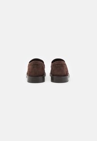 Brune semskede loafers med en glat sort sål, der har en syet søm og et lavt profildesign uden synlige hardware eller pynt.