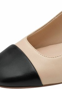 Chaussure plate en cuir beige avec un bout en cuir noir. Présente une forme arrondie et une texture lisse, avec des coutures visibles le long des bords.