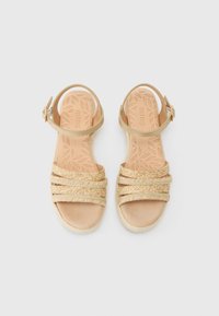 Beige woven sandals with four textured straps and an ankle buckle. The insole features a leaf pattern, with a slight wedge heel.