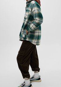 Giacca in pile a quadri verde e bianca con colletto, tasche laterali e un'etichetta. Pantaloni in corduroy marroni con vestibilità ampia e tasche cargo.