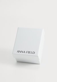 Biały pudełko papierowe z pokrywą, z napisem "ANNA FIELD" czarnymi literami. Gładka faktura i prosty design, kwadratowy kształt z kanciastymi rogami.