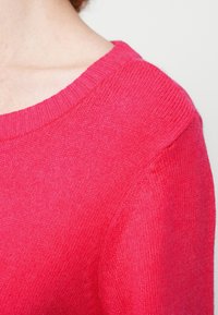 Φούξια πλεκτό πουλόβερ με ριμπ λαιμόκοψη και απαλή υφή. Διαθέτει ελαφρώς χαλαρή εφαρμογή και ομαλή επιφάνεια στο ύφασμα.