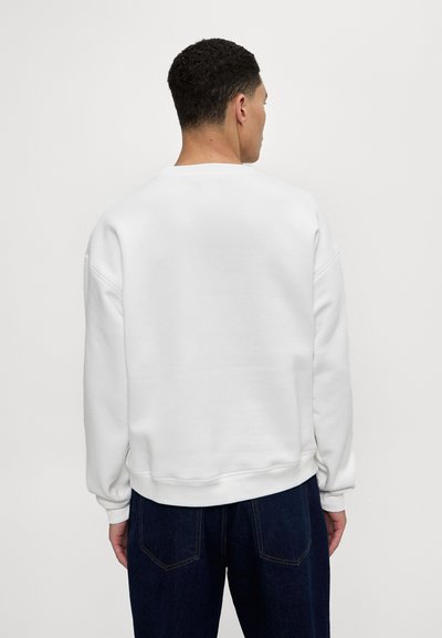 Sweat-shirt en polaire blanche à coupe décontractée, encolure ronde, avec des poignets et un ourlet côtelés, associé à un jean en denim foncé.
