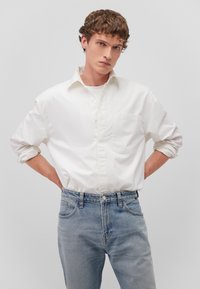 White long-sleeve button-up shirt with a chest pocket, paired with light blue denim jeans, featuring a classic fit and rolled-up sleeves.