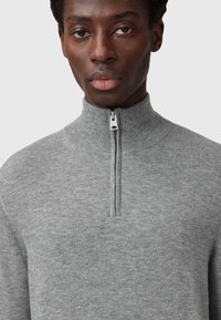 Maglione grigio con zip e collo alto realizzato in morbido tessuto a maglia. Presenta una texture sottile e un piccolo logo vicino al petto.