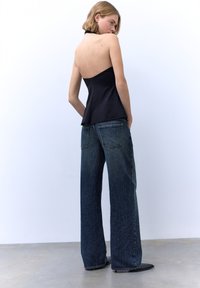 Musta halterneck-toppi, jossa on vartalonmyötäinen yläosa, yhdistetty leveälahkeisiin tummiin farkkuihin, joissa on kontrastiväriset saumat ja hieman kulunut viimeistely.