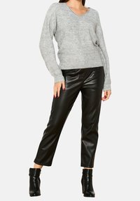 Grauer V-Ausschnitt-Pullover mit langen Ärmeln, kombiniert mit schwarzen Lederhosen und Stiefeletten, mit einer taillierten Silhouette und glatter Textur.