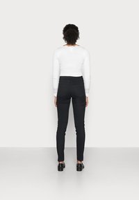 Jeans skinny neri con vita alta, tessuto elasticizzato morbido e vestibilità slim. Abbinati a un top bianco a maniche lunghe con dettagli in pizzo.