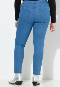 Vaqueros de mezclilla azul con corte slim, con bolsillos traseros y una textura suave. Combinados con botas de tobillo plateadas y brillantes.