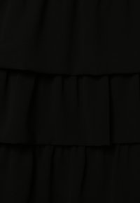 Musta mekko kerroksittain neulottuilla röyhelöillä. Pehmeä kangastunne, jossa on kolme tasoa. Yksinkertainen muotoilu ilman ylimääräisiä kuvioita tai koristeita.