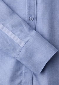 Poignet de chemise bleu clair à manches longues avec un détail à rayure blanche et un bouton bleu visible sur la patte de la manche.