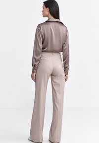 Jedwabista, jasnobrązowa koszula z długim rękawem i kołnierzykiem, zestawiona z beżowymi, wąskopaskowymi spodniami o wysokim stanie i szerokich nogawkach. Gładka tekstura, dopasowany krój.