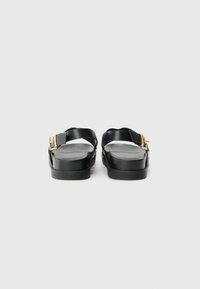 Black leather sandals with a flat sole, featuring a strap and gold buckle detail. Smooth texture and minimalistic design.
