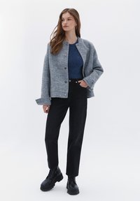 Grå ullblandad jacka med silverknappar, kombinerad med en blå topp och svarta högmidjade jeans. Modellen bär svarta snörstövlar.