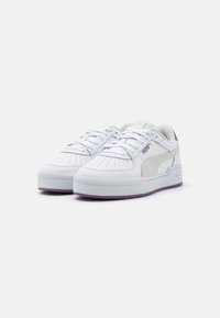 Sneakers bianchi con tomaia in pelle liscia, punta perforata e dettagli viola. Presentano una suola spessa e lacci piatti. Marchio PUMA visibile.