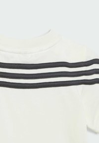 T-shirt bianca con collo a giro, caratterizzata da tre righe nere nella zona delle spalle. Tessuto morbido con un design semplice.