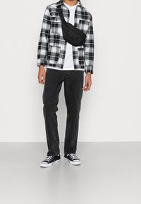 Svart och vit rutmönstrad flanellskjorta, vit T-shirt, svarta jeans och svarta sneakers med vita accenter; svart axelremsväska.