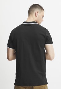 Černé polo tričko s krátkými rukávy, s bílým lemováním kolem límce a okrajů rukávů, hladký materiál a klasický střih.