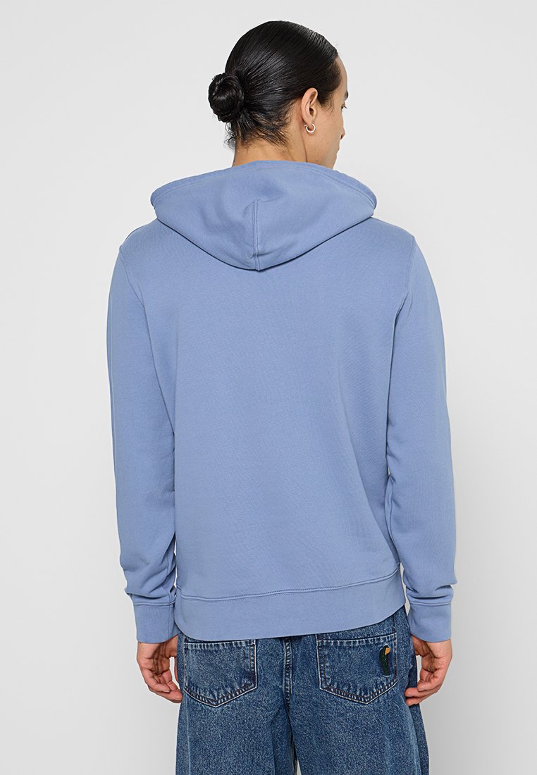 Sudadera azul claro hecha de tejido suave, con una gran capucha, puños acanalados y un dobladillo recto. Sin logotipos ni patrones visibles.