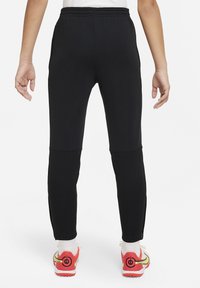 Schwarze Sporthosen mit schmalem Schnitt, elastischem Bund und Paneelakzenten; getragen mit leuchtend farbigen Schuhen.